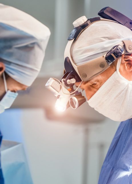 Process of surgery operation using medical equipment. Two surgeons in operating room with surgery equipment and in binocular glasses. Medical background.